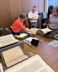 Several people stand around a large wooden table covered in early books and manuscripts sitting on foam cushions.