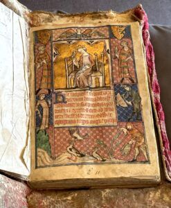 An illuminated medieval manuscript showing a crowned man sitting and holding a hawk or falcon on one gloved arm. Around him are illustrations of falconry practices. In the center of the page is some text in Latin.